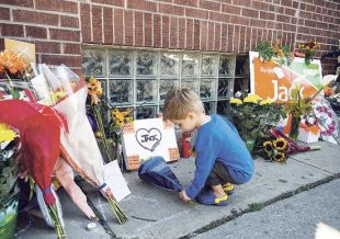 Harlan Bennett, 2, places some flowers Tuesday at the NDP office in Toronto that has become a shrine to the late NDP leader Jack Layton. — Photo by The Canadian Press